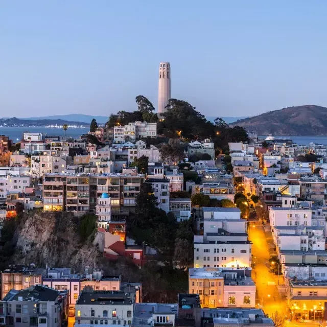 黄昏时分的贝博体彩app科伊特塔, with lighted streets before it and the San Francisco Bay behind it.